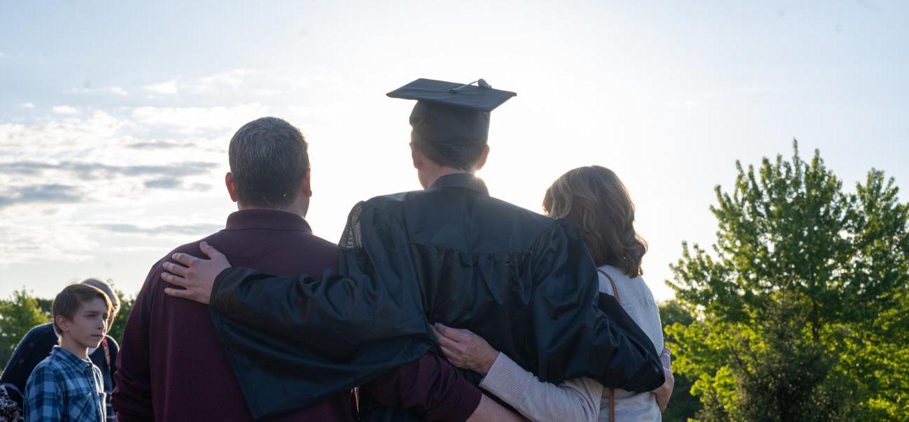 An Ohio University student poses wearing their cap and gown, with their parents by their side